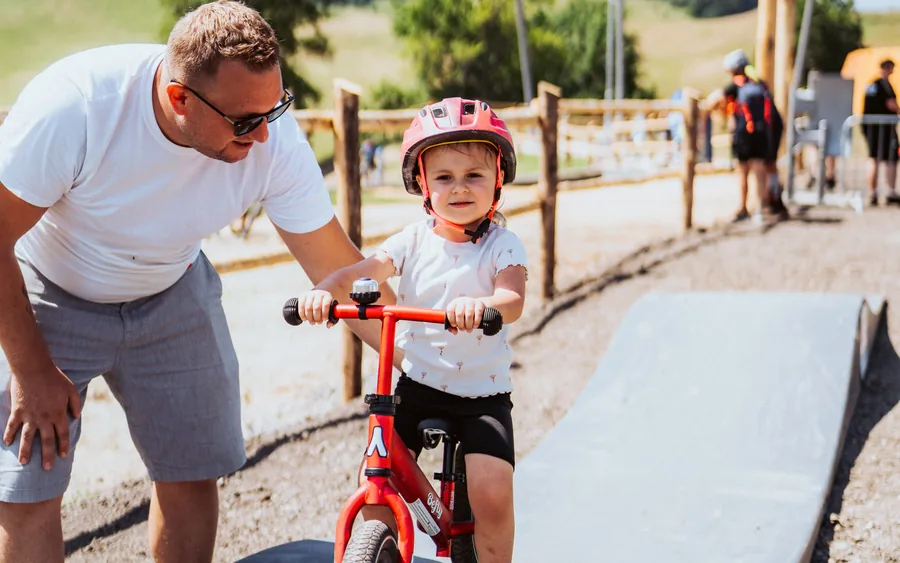 Malé dievčatko na odrážadle na modulárnom pumptracku, oco ho pridržiava pri štarte