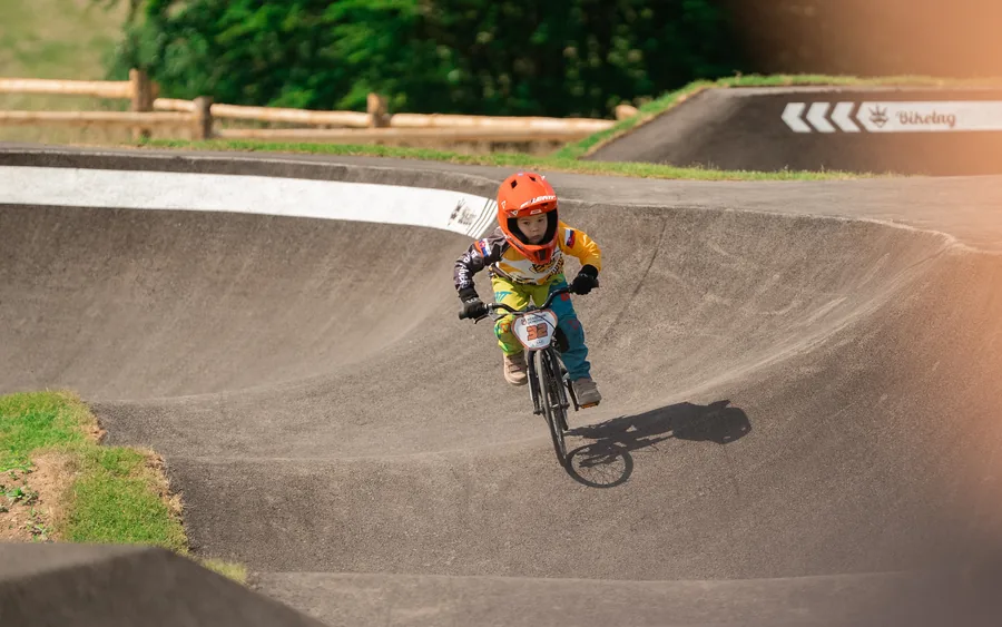 Dieťa v oranžovej prilbe pretekárskym štýlom prechádza vlnu na pumptracku v Riders Park Donovaly